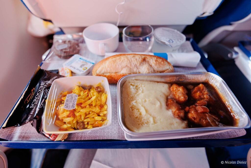 Plateau-repas servi à bord d'un vol Air Caraïbes, comprenant un plat chaud, des pâtes, du pain et des desserts.