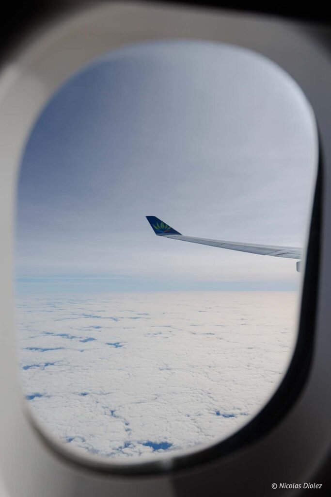 Vue depuis le hublot d'un avion Air Caraïbes survolant une mer de nuages lors du vol inaugural vers Saint-Martin.