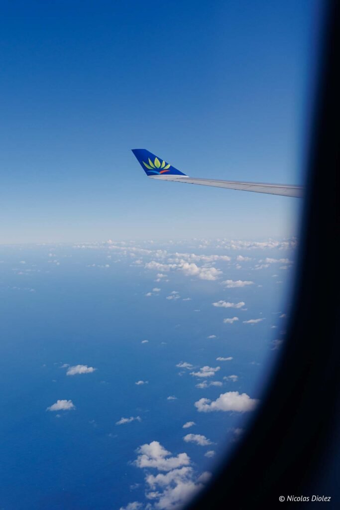 Aile d'un avion Air Caraïbes en vol au-dessus de nuages et de l'océan lors du vol inaugural vers Saint-Martin.