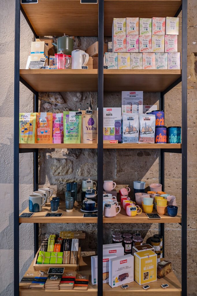 Wooden shelving of a Malongo boutique presenting teas, Marta coffees, barista accessories, and organic pastries on the shelf.