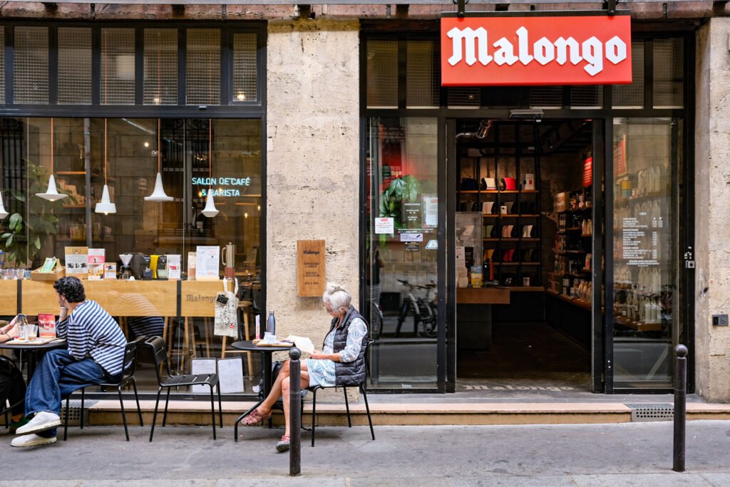 Terrace of the Malongo coffee shop and barista with customers sitting in front of the shop.