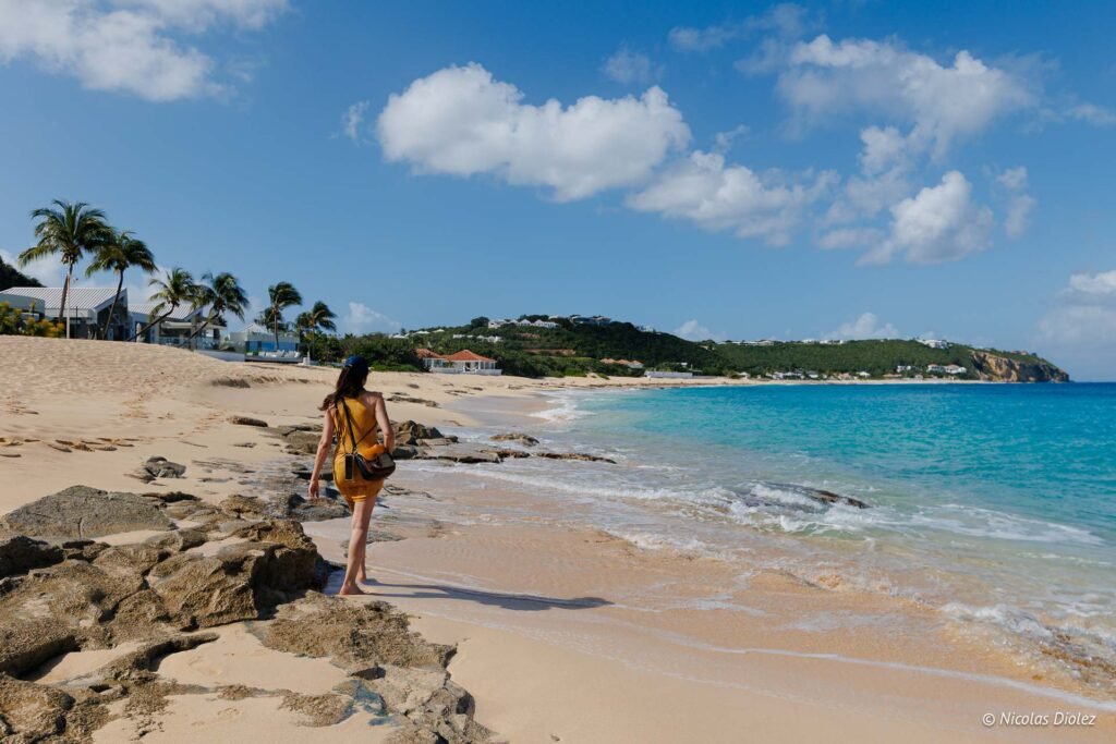 Femme marchant seule sur le sable de la plage de Baie Rouge à Saint-Martin avec une mer turquoise.