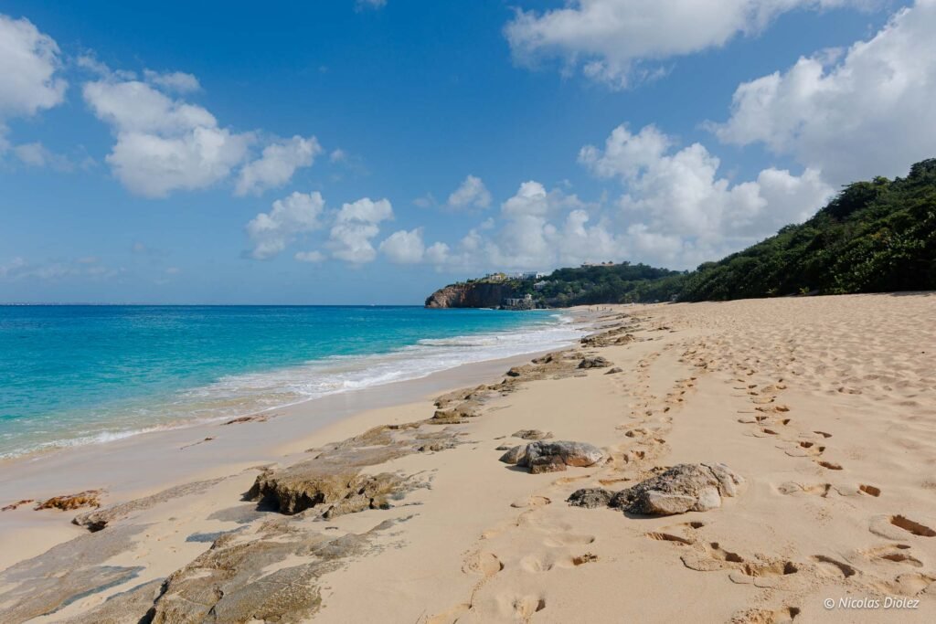 Plage de Baie Rouge à Saint-Martin avec son sable fin, ses rochers et la mer turquoise sous un ciel nuageux.