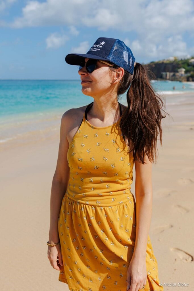 Femme souriante en robe jaune et casquette sur la plage de Baie Rouge.