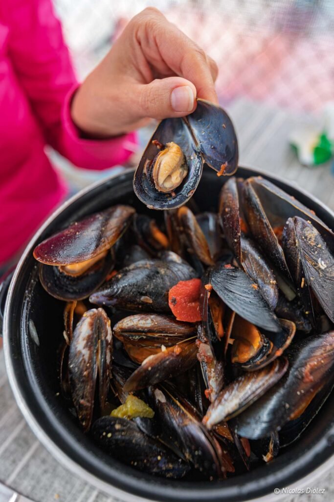 Main tenant une moule cuisinée au-dessus d'une marmite pleine de moules façon Coquille à l'étang de Thau.