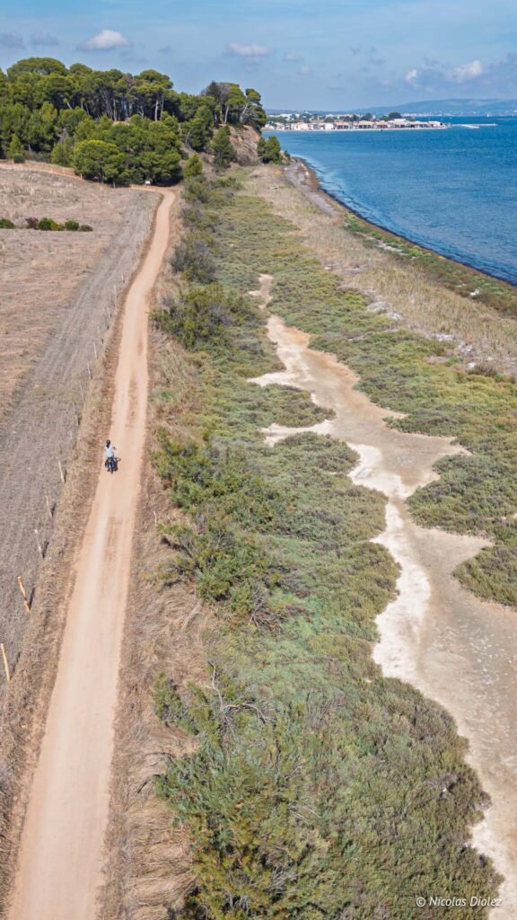 Cycliste sur un chemin côtier à Sète, entre végétation méditerranéenne et étang de Thau, vue par drone.