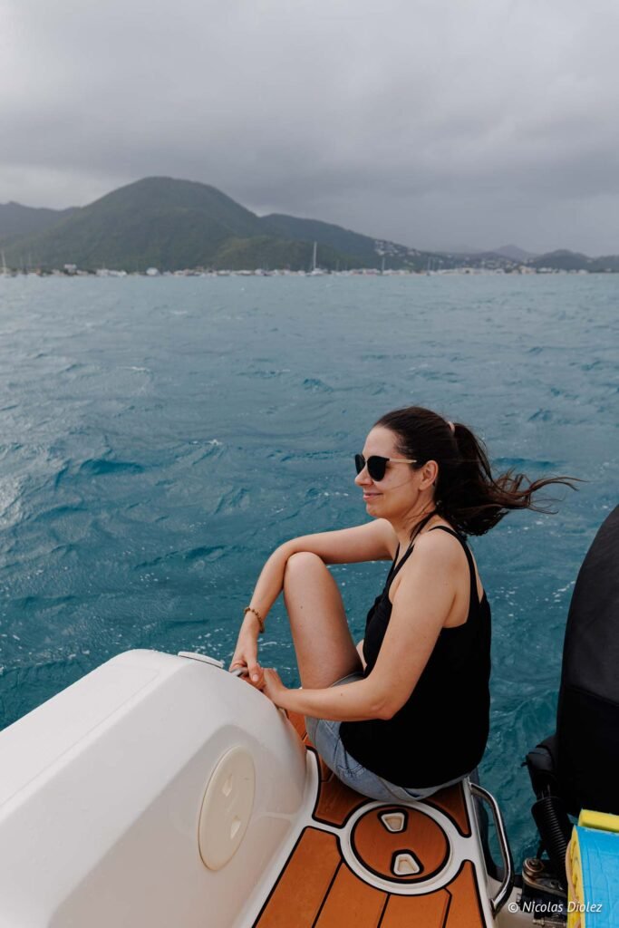 Femme souriante en excursion en bateau à Saint-Martin avec vue sur la mer et les montagnes.
