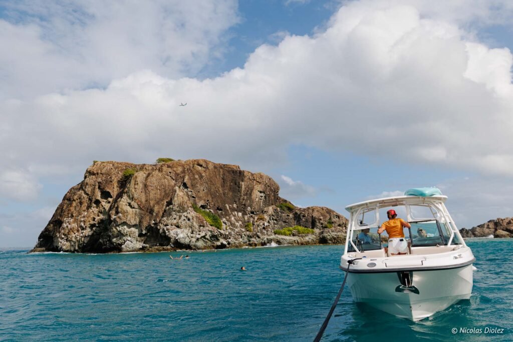 Excursion en bateau à Saint-Martin avec des touristes nageant près d'un îlot rocheux.