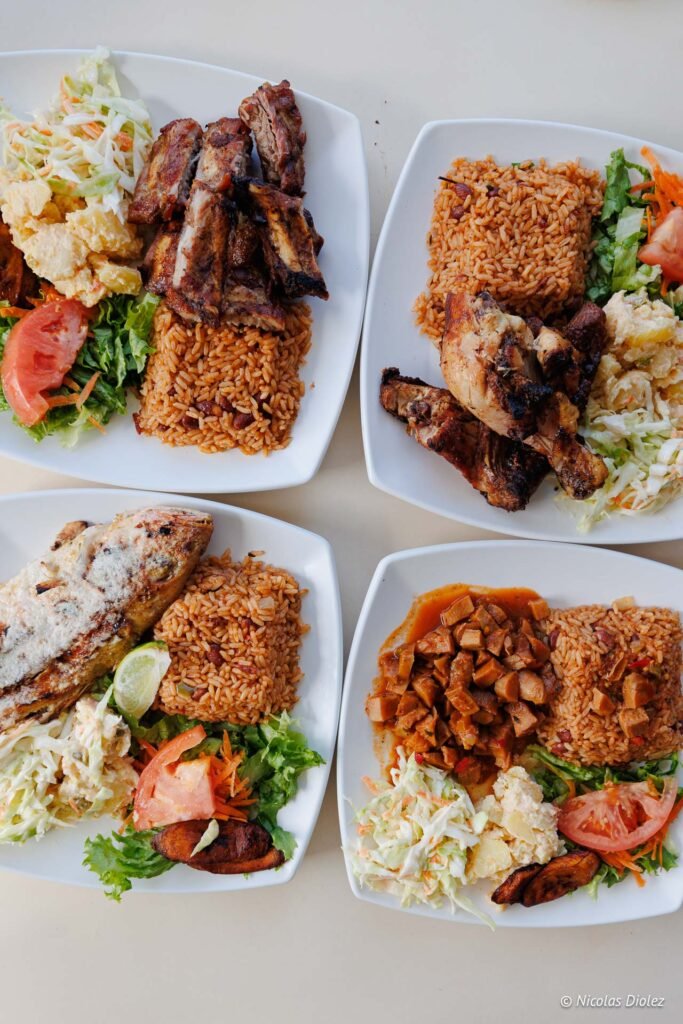 Quatre assiettes de plats antillais traditionnels avec du poulet grillé, du poisson, du riz et des bananes plantain à Grand-Case.