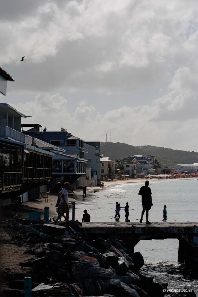 Personnes se promouvant sur la plage et le ponton à Grand-Case, Saint-Martin, sous un ciel nuageux.