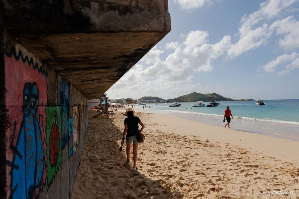 Promeneuse marchant sur la plage de sable à Grand-Case, Saint-Martin, le long d'un mur en béton orné de graffitis.