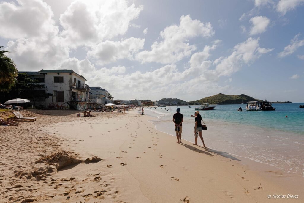 Promeneurs sur la plage de sable fin de Grand-Case à Saint-Martin, bordée de bâtiments et de la mer des Caraïbes.