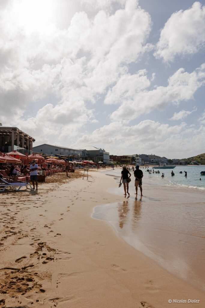 Personnes marchant sur la plage de Grand-Case à Saint-Martin avec des parasols et la mer des Caraïbes.