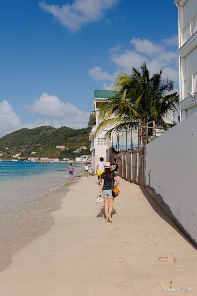Promeneurs marchant sur la plage de sable fin à Grand-Case à Saint-Martin, le long des bâtiments et de la mer des Caraïbes.