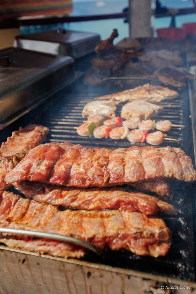 Côtes de porc et brochettes de crevettes en train de cuire sur un barbecue à Grand-Case, Saint-Martin.