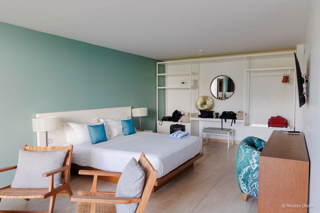 Suite lumineuse avec lit king-size, coin bureau, étagères murales et fauteuils en bois à l'hôtel Hommage Saint-Martin.