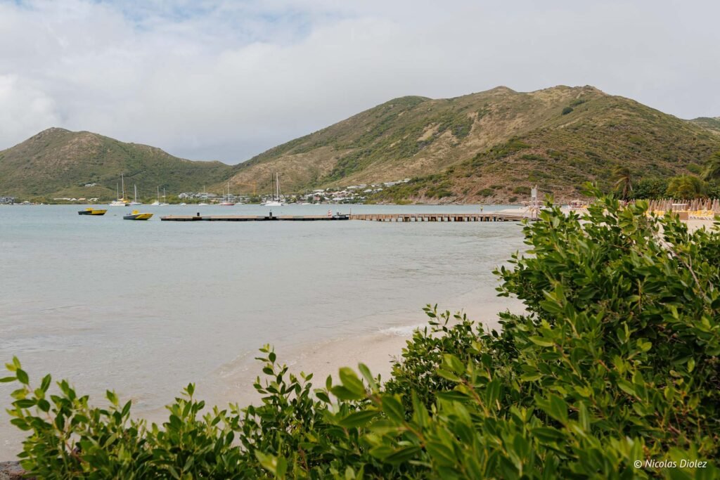 Jetée sur la plage de l'Îlet de Pinel à Saint-Martin avec des collines verdoyantes en arrière-plan.