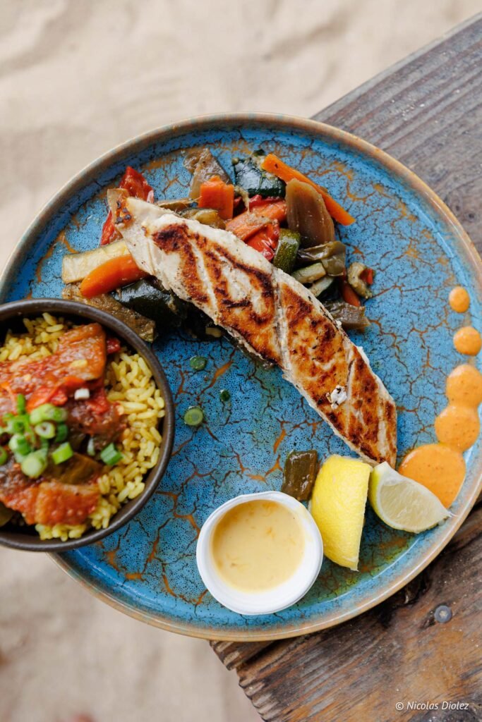 Plat de poisson grillé servi avec des légumes, du riz épicé et des quartiers de citron à l'Îlet Pinel.