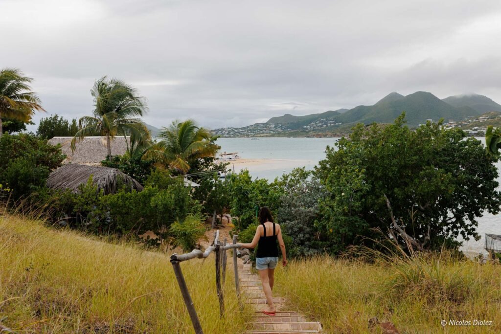 Femme marchant sur un sentier en pente menant à la plage de l'îlet Pinel sous un ciel nuageux.