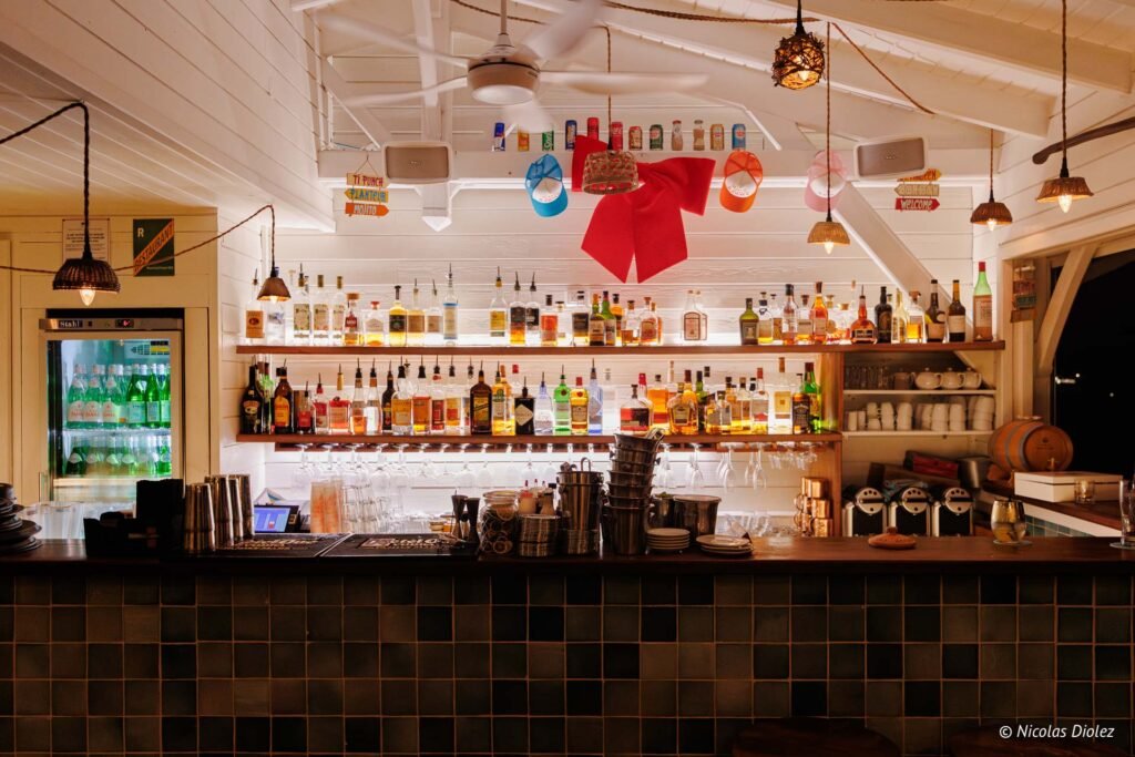 Comptoir de bar garni de bouteilles d'alcool et étagères illuminées au restaurant Le Temps des Cerises à Saint-Martin.