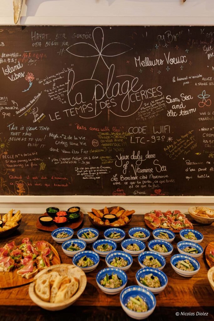 Buffet de tapas et petits bols devant un grand tableau noir décoré d'inscriptions à la craie au restaurant Le Temps des Cerises à Saint-Martin.