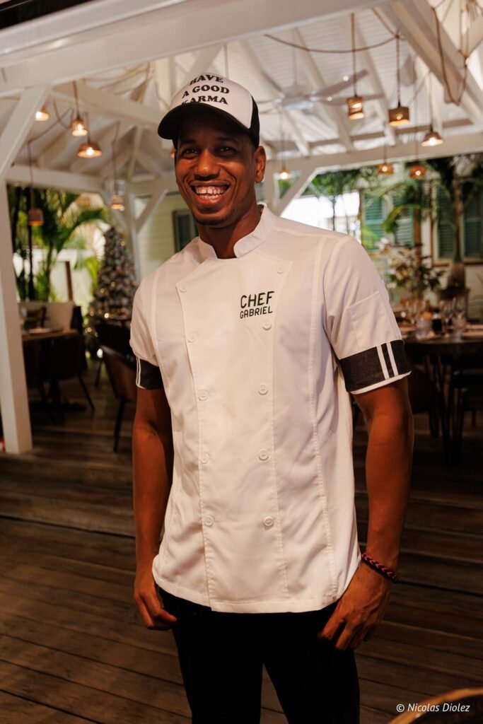 Chef Gabriel souriant portant une veste de cuisine blanche et une casquette au restaurant Le Temps des Cerises à Saint-Martin.