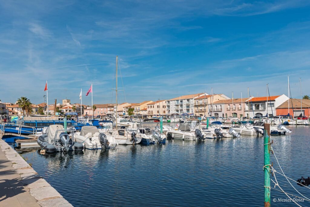 Bateaux amarrés dans le port de plaisance de Mèze, avec les façades des maisons en arrière-plan sous ciel bleu.