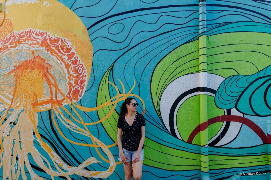 Touriste posant devant une grande fresque murale colorée représentant une méduse en partie hollandaise à Saint-Martin.