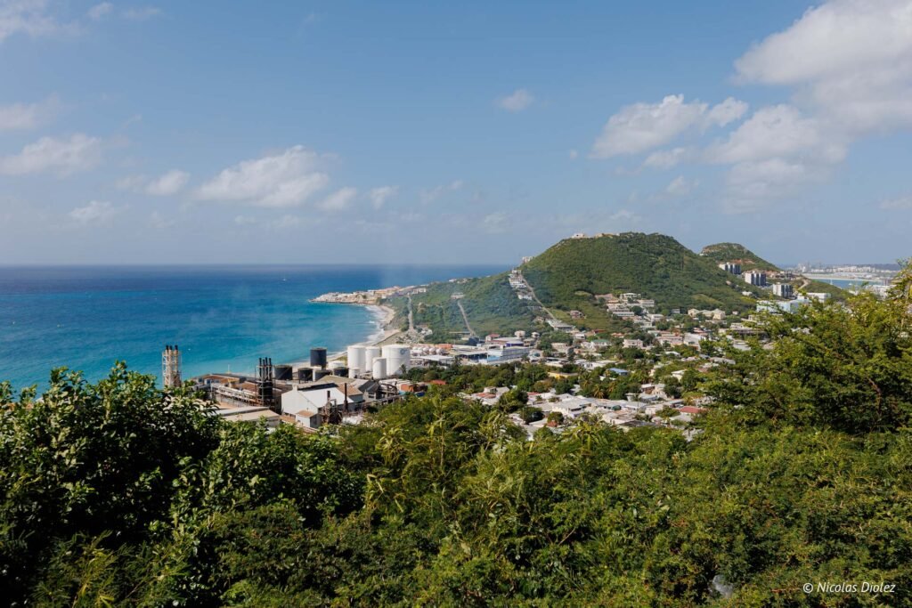 Vue panoramique sur la partie hollandaise de Saint-Martin avec une zone industrielle côtière et des collines verdoyantes.