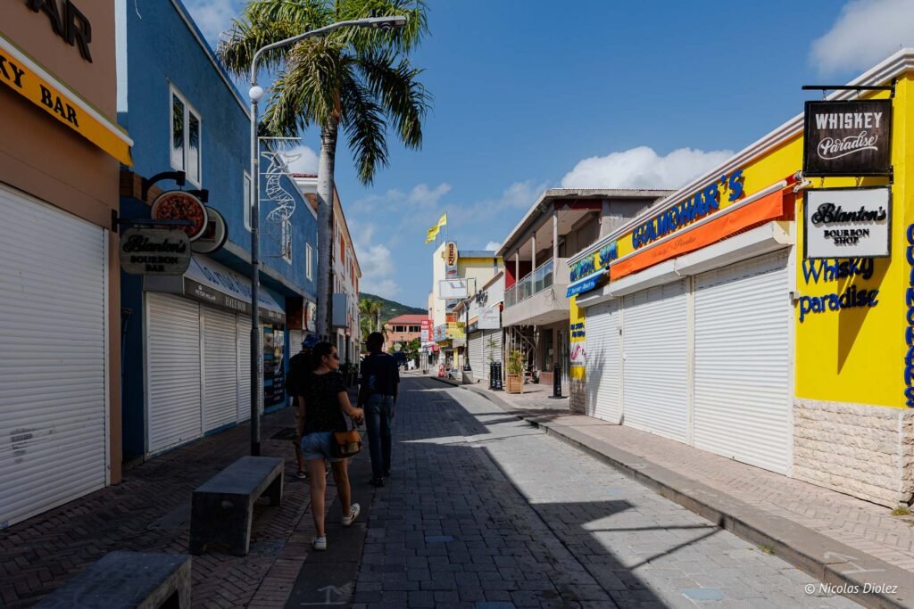 Piétons marchant dans une rue commerçante de la partie hollandaise de Saint-Martin bordée de boutiques aux façades colorées.