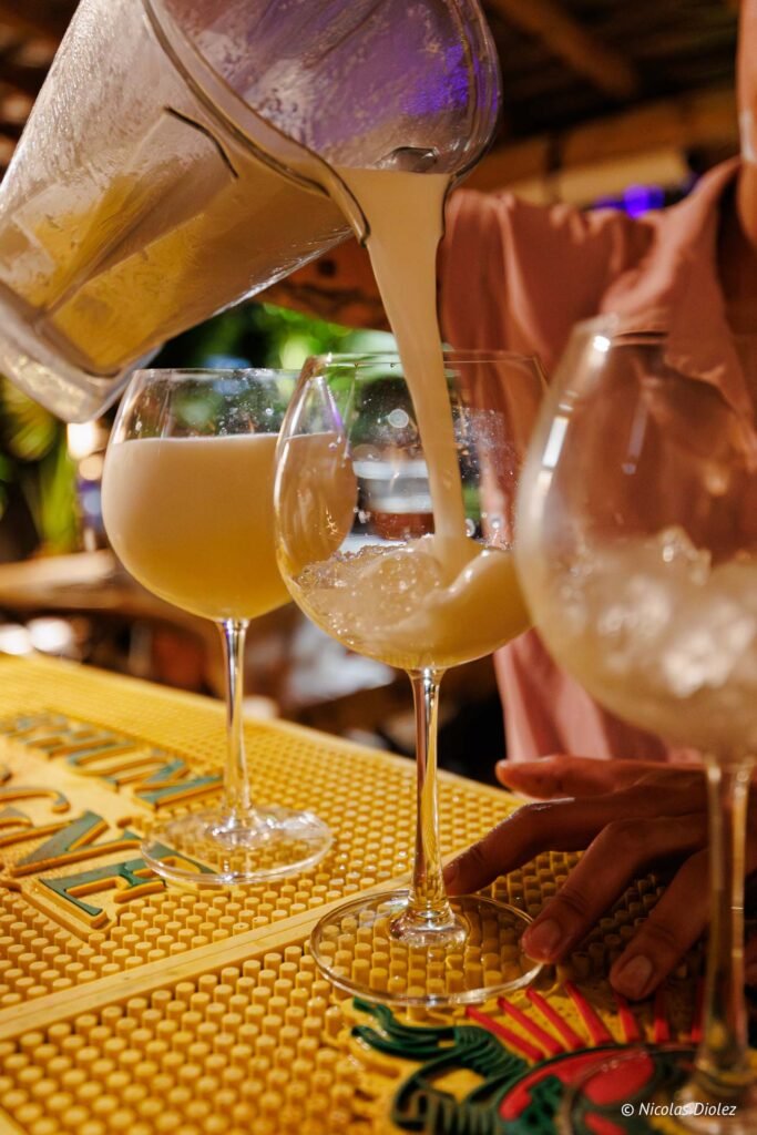 Un barman verse un cocktail crémeux d'un blender dans des verres à pied remplis de glaçons lors d'une soirée à l'Hôtel Hommage Saint-Martin.