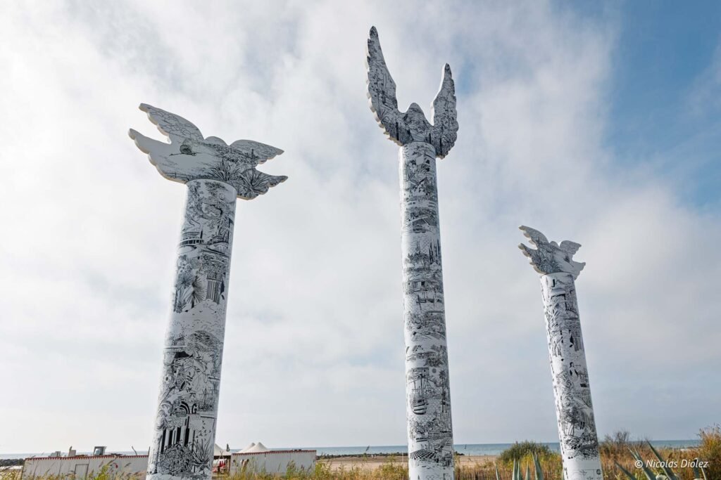 Trois colonnes artistiques sculptées en forme d'oiseaux sur la plage à Sète lors d'une balade à vélo.