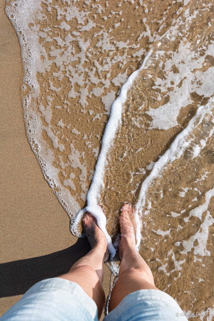 Pieds nus sur le sable mouillé bordés par l'écume des vagues sur une plage près de Sète.