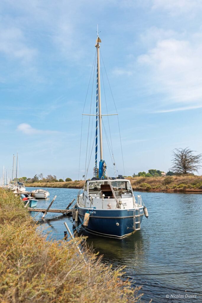 Voilier amarré le long d'un canal près de Sète, entouré de végétation.