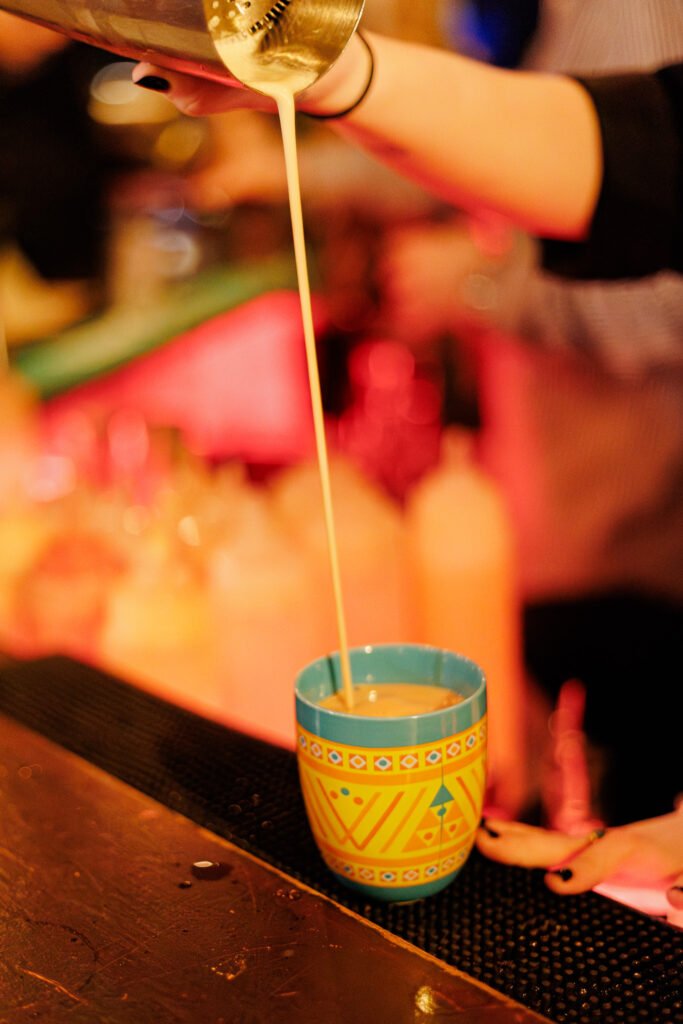 Ein Bartender gießt einen Botran-Rum-Cocktail aus einem Shaker in ein buntes Glas.