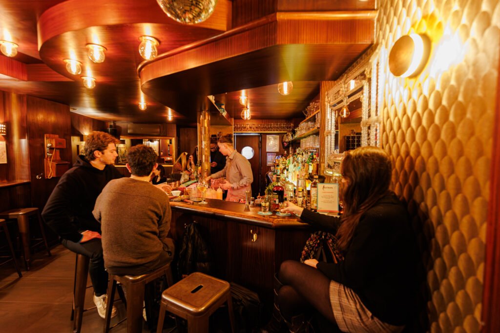 Gäste sitzen am Tresen einer gemütlichen Bar, während ein Bartender Botran-Cocktails zubereitet.