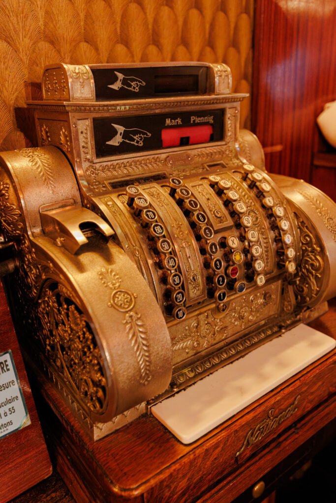 Alte mechanische Registrierkasse aus goldfarbenem Metall mit nummerierten Tasten und Vintage-Ornamenten.