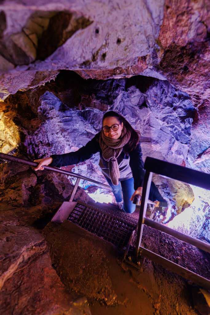 Female visitor walking up metal stairs inside the illuminated Saulges caves.