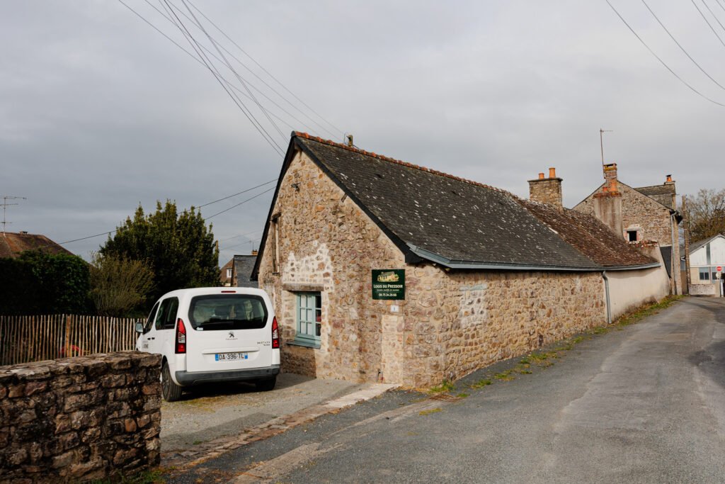 Stone facade of Le Logis du Pressoir gîte in Sainte-Suzanne with a white van parked outside.