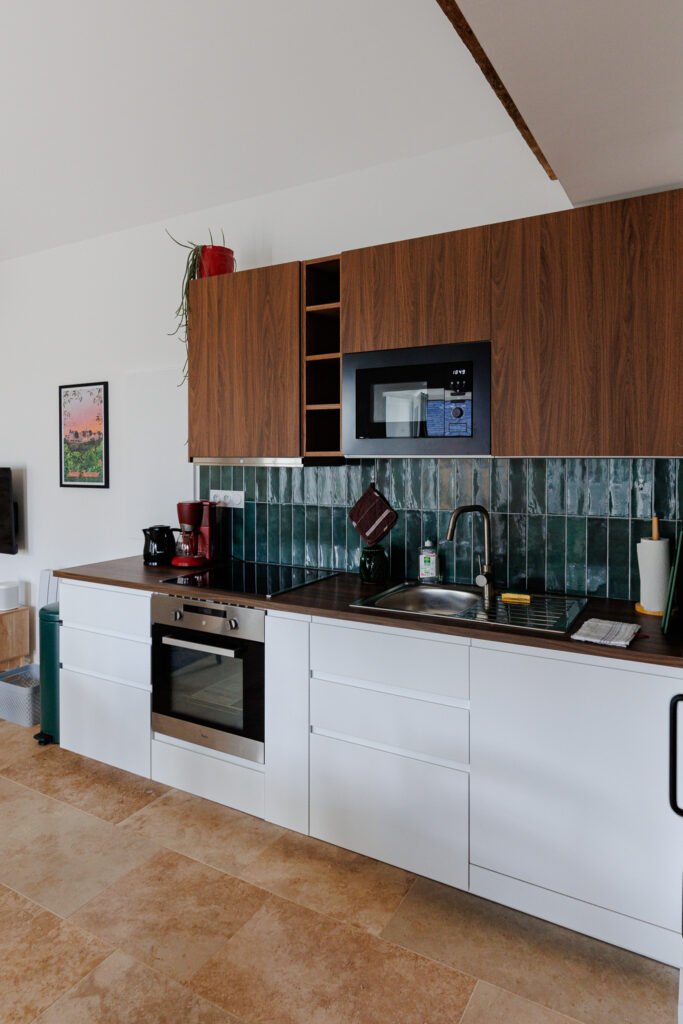 Modern kitchen with white base cabinets, wooden cupboards, green tiled backsplash, and built-in appliances.