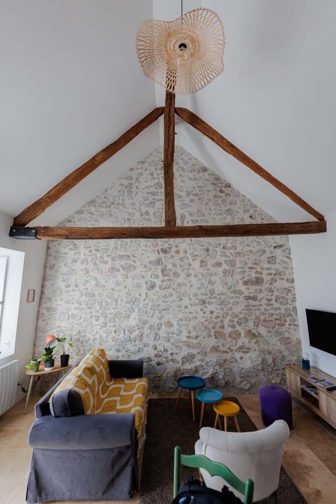 Bright living room with exposed stone walls, wooden beams, and exposed framework at Le Logis du Pressoir in Sainte-Suzanne.