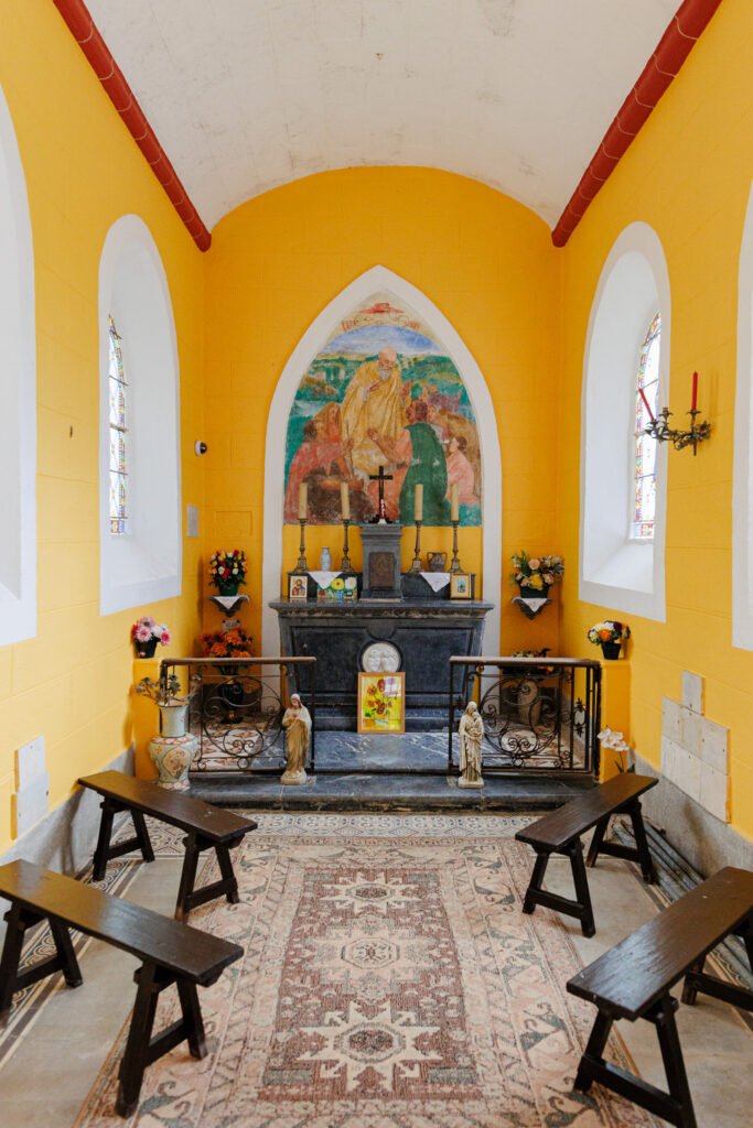 Interior of the Saint-Céneré oratory with its yellow walls, stone altar, and wooden pews.