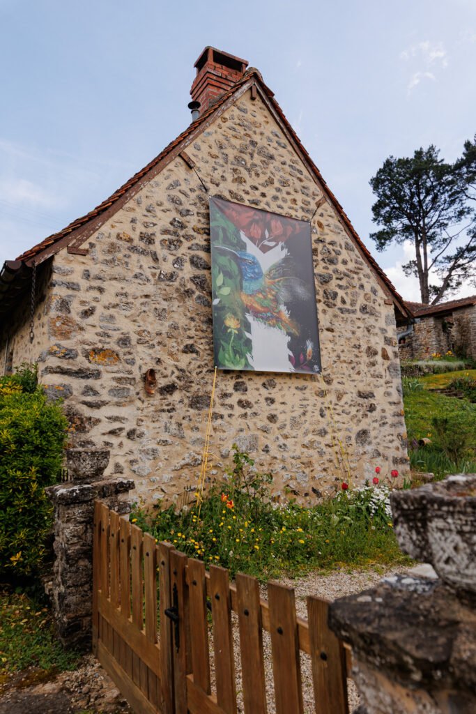 Large artistic banner hung on the stone facade of an old house in Saint-Pierre-sur-Erve.