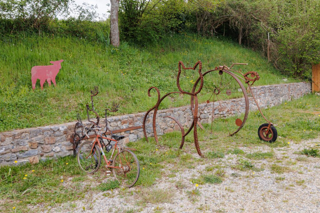 Rusted metal sculptures representing a cat and a large vintage bicycle in a garden in Saint-Pierre-sur-Erve