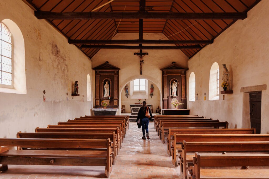 Interior of the Saint-Pierre-sur-Erve church with its wooden pews and a person walking toward the altar.