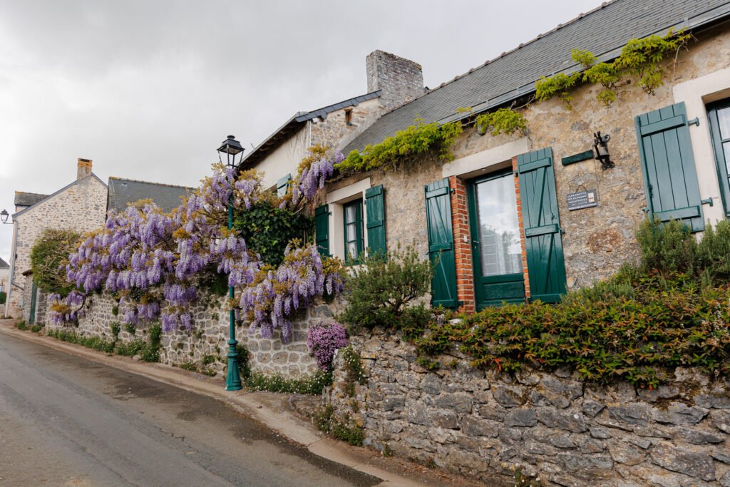Traditional stone house with green shutters and blooming wisteria along a street in Saint-Pierre-sur-Erve.