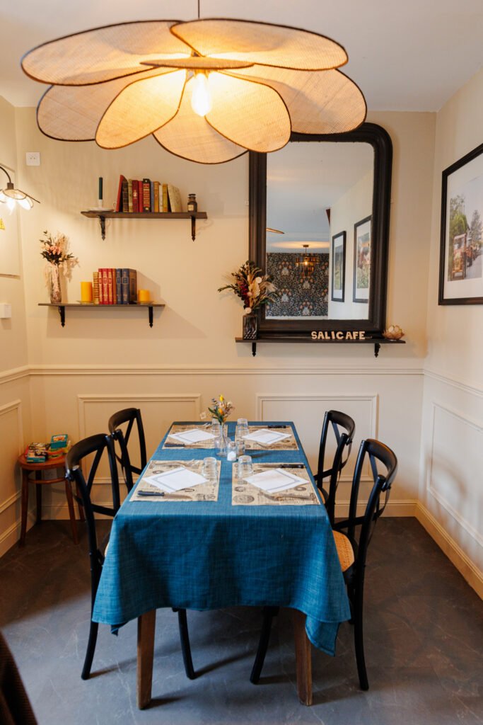 Warm interior of a restaurant with a set table, large floral hanging arrangement, bookshelves, and a large mirror.