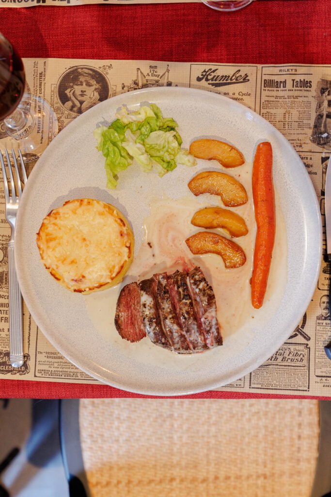 Plate with sliced roast beef in sauce, potato gratin, carrot, apple wedges and green salad.