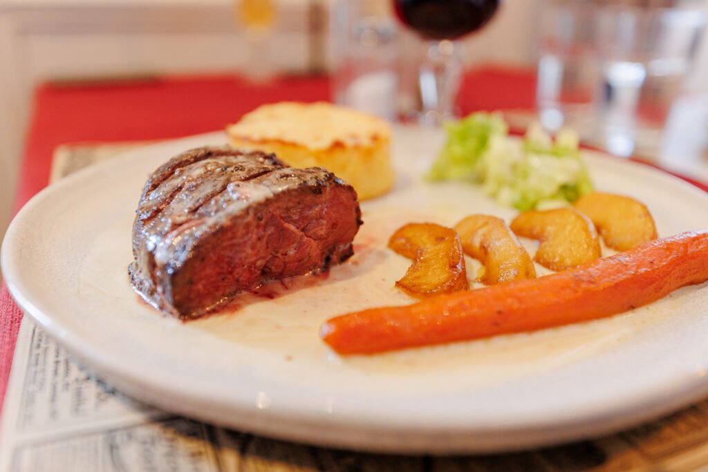 Plate with a sliced tender steak, roasted carrot, potatoes, and vegetables.