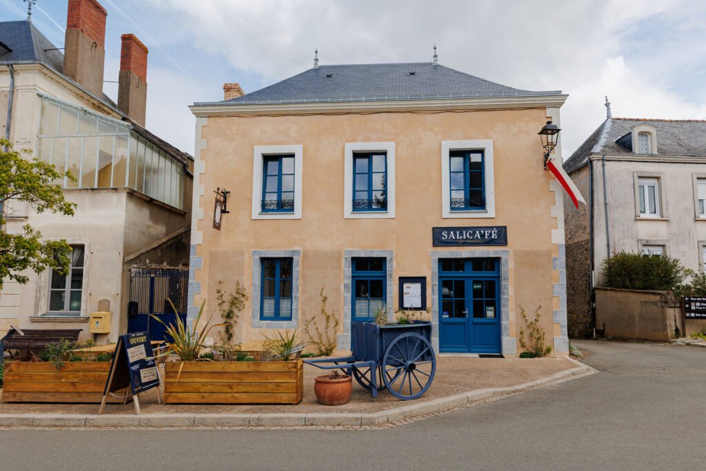 Facade of the Salicafé with blue windows and a decorative old cart on the village square.